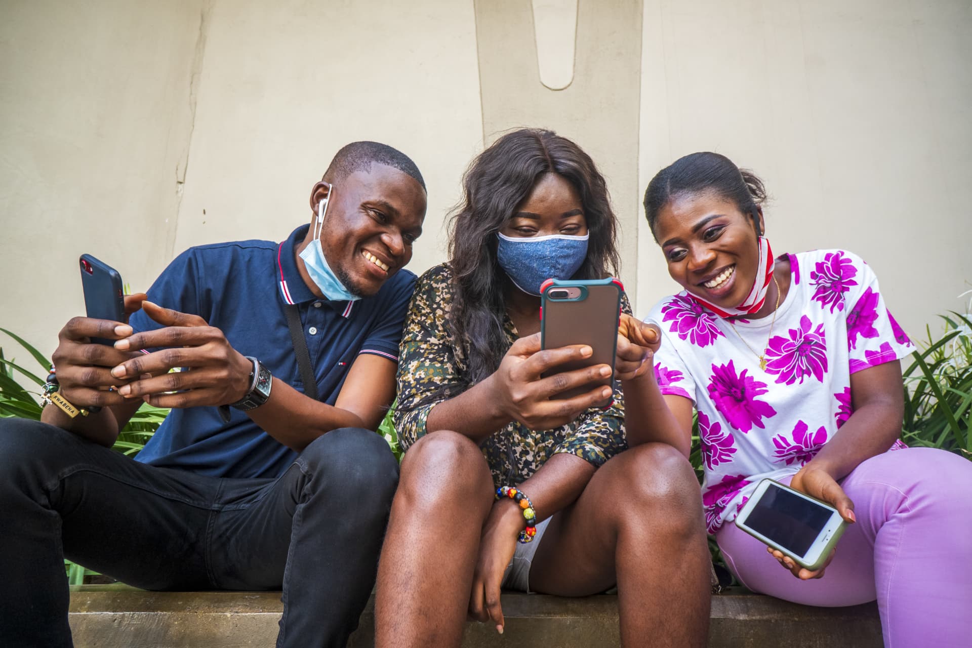 Three young friends sitting together, smiling and using their phones to access health information