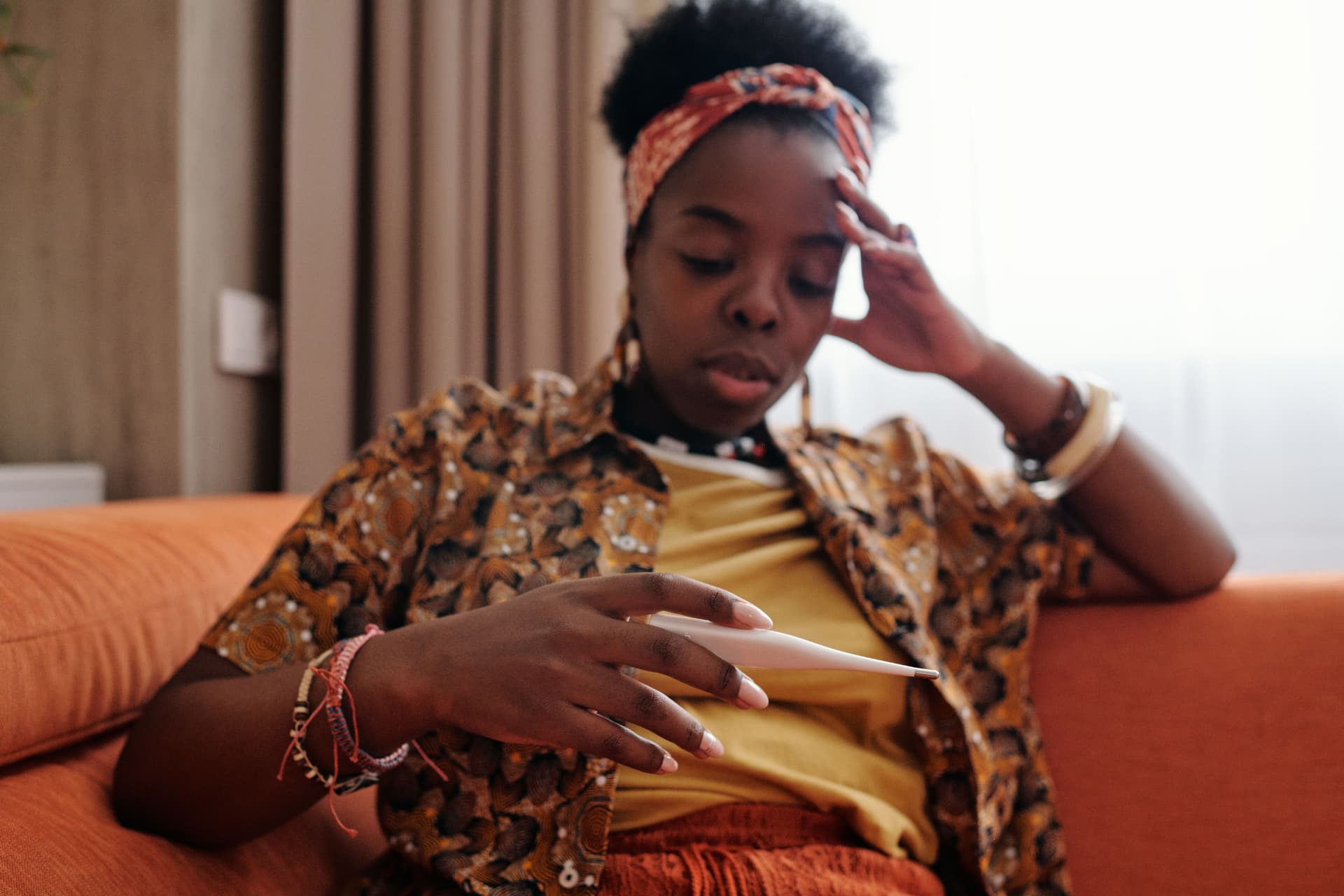 A person resting on a sofa while checking their temperature, showing everyday health monitoring at home