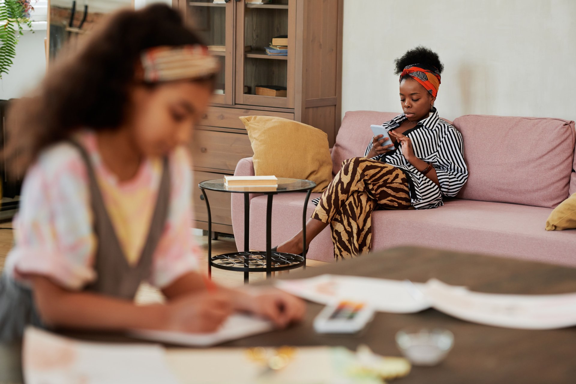 A woman reviewing health information on her phone at home while a child studies nearby