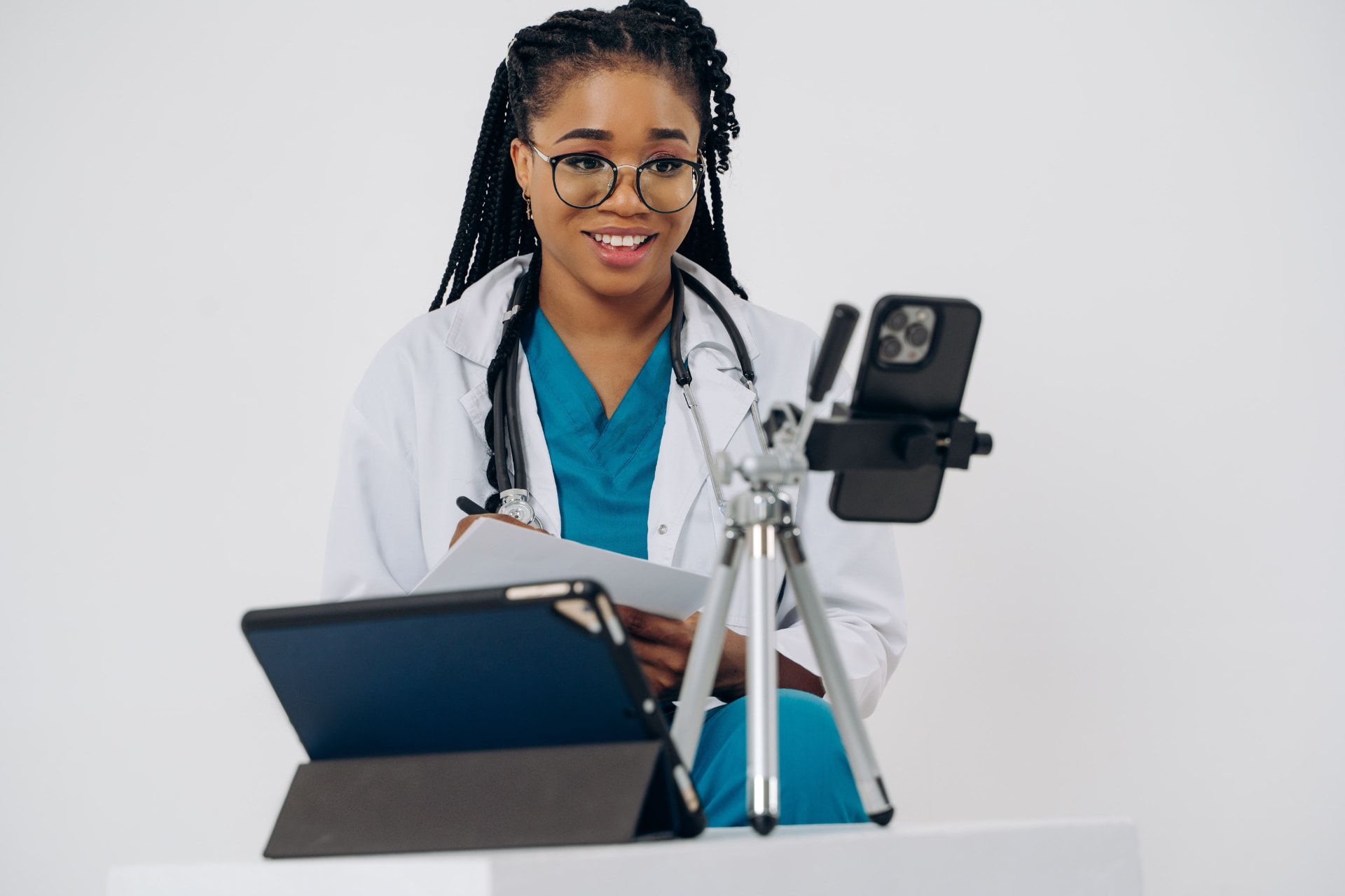 A healthcare professional consulting with a patient through a phone and tablet setup